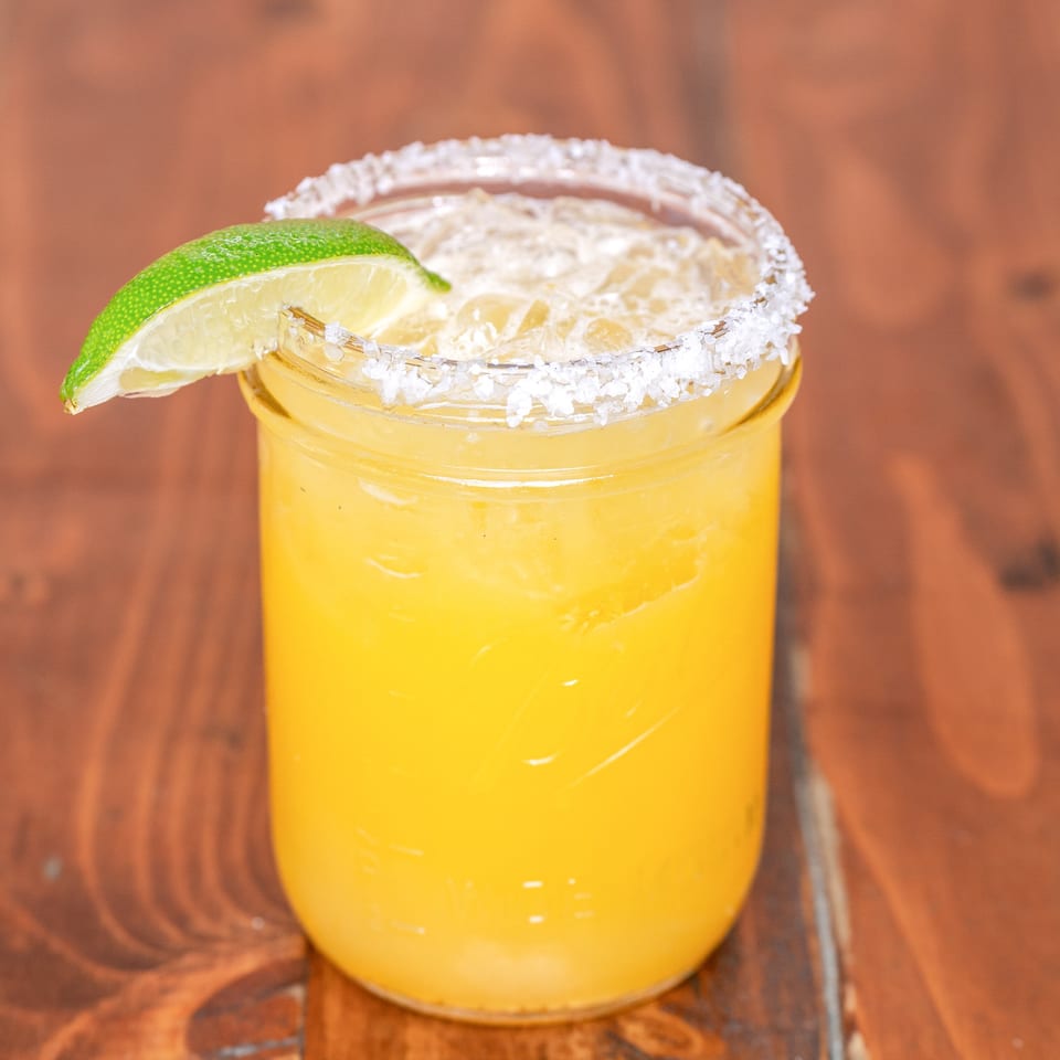 A Que Pasa Cantina margarita in a mason jar with a salted rim and lime wedge.