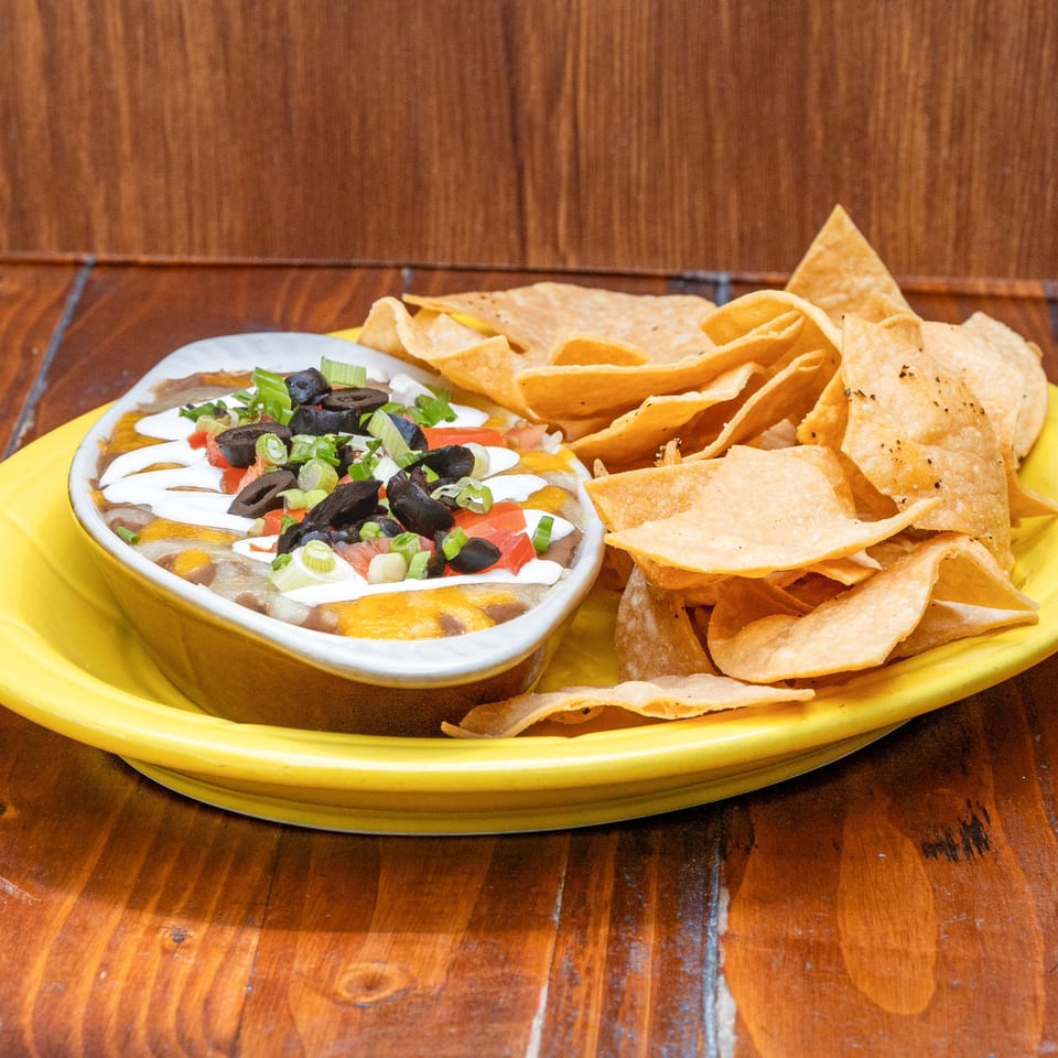 Que Pasa Cantina's 7-layer dip with sour cream, olives, tomatoes, and green onions, served with tortilla chips.
