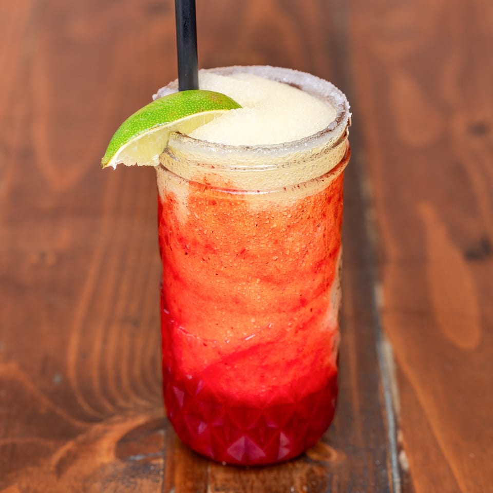 Que Pasa Cantina's layered strawberry and lime frozen margarita with a salted rim and lime wedge.